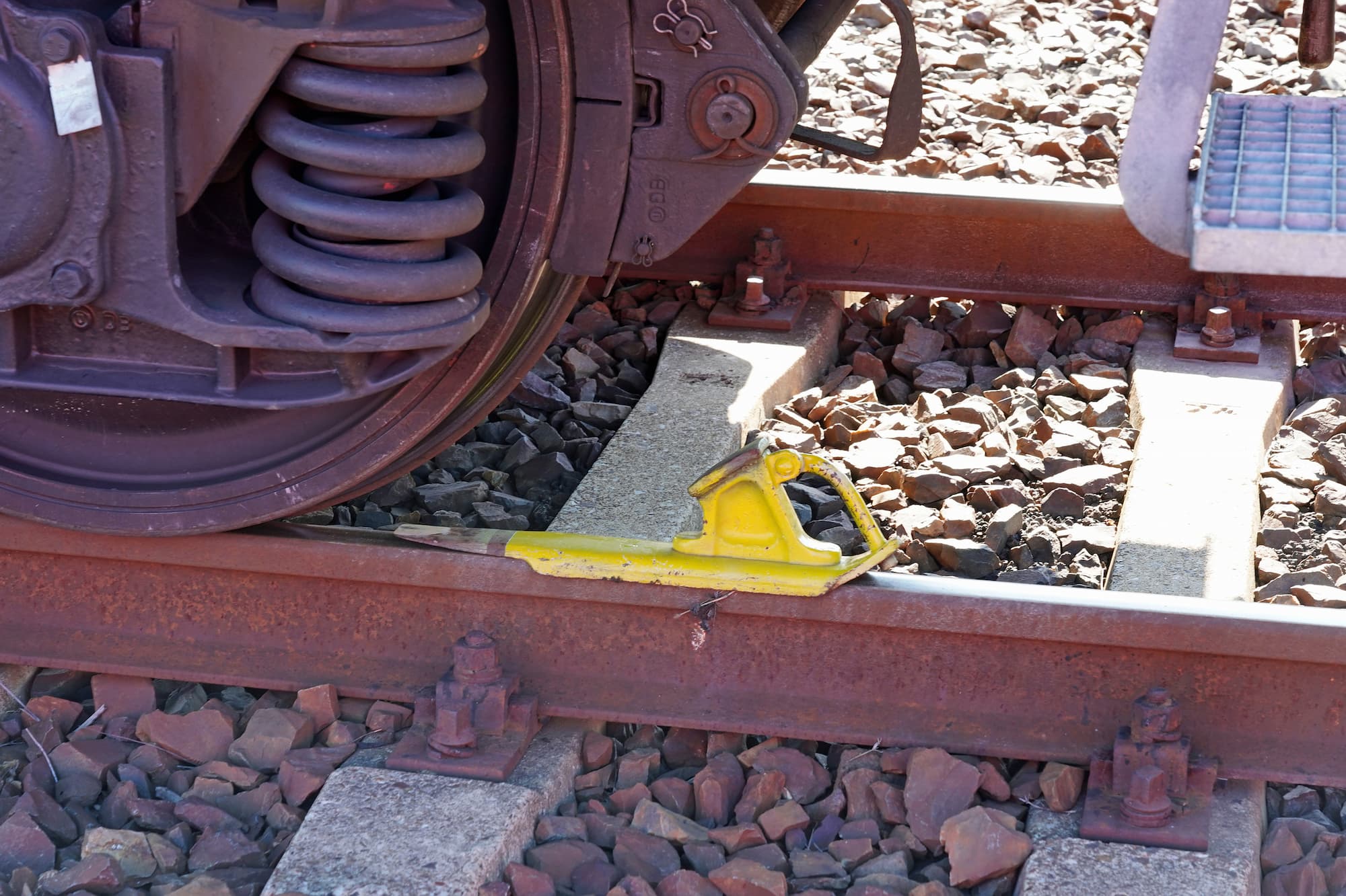 Ein Einheits-Hemmschuh bremst ein Wagenrad auf einem Gleis.