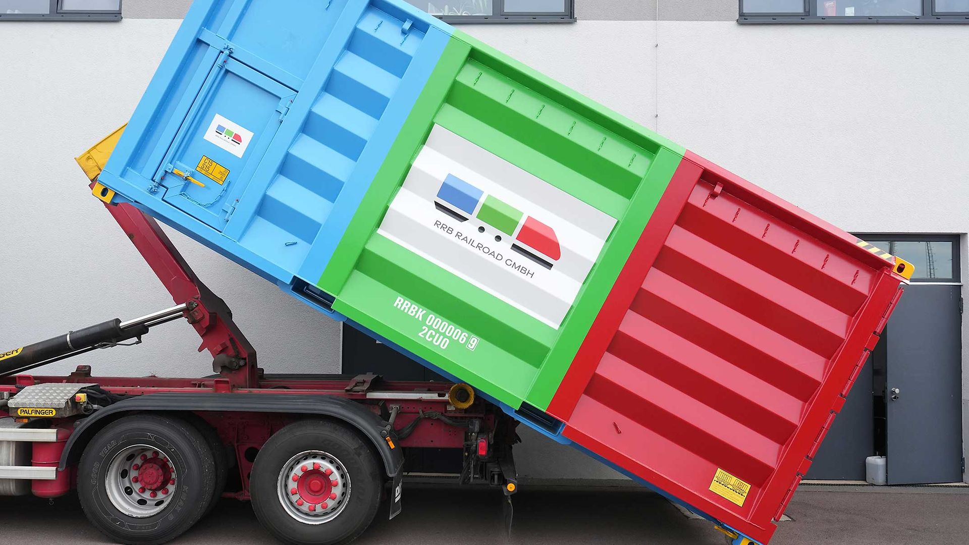 Ein Container (blau, rot und grün) steht auf einem Lkw.