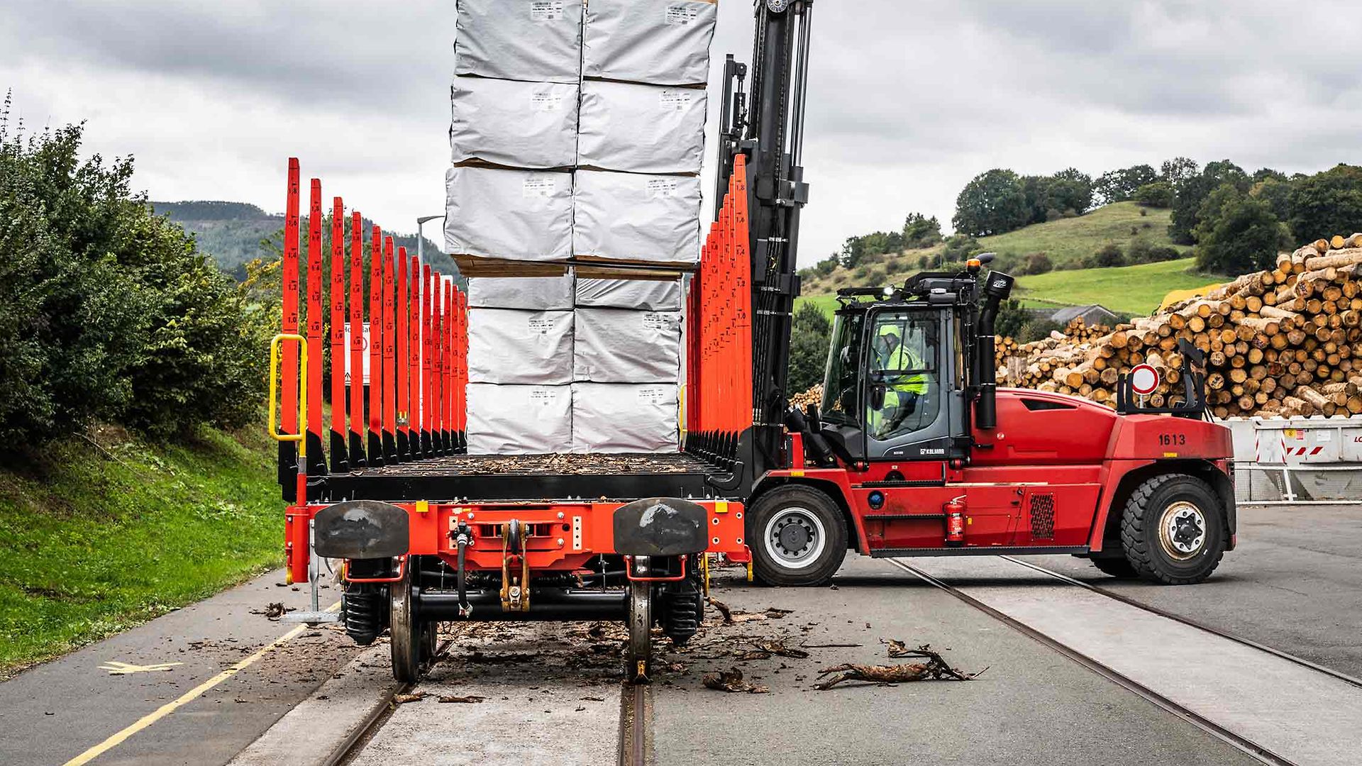 Ein Hubwagen belädt einen Rungenwagen mit in Folie eingepackten Holzlatten.