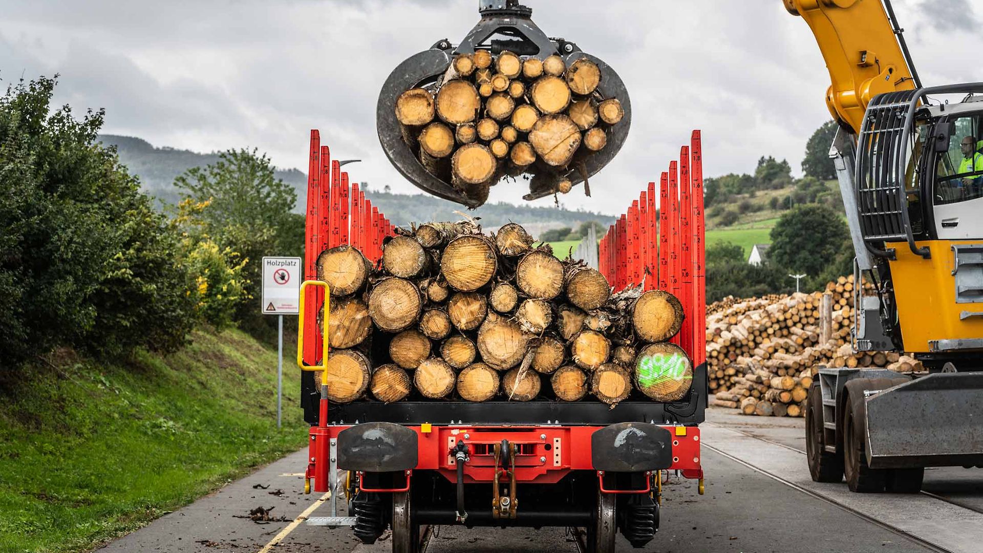 Ein von hinten zu sehender Rungenwagen wird mit Rundholz beladen.