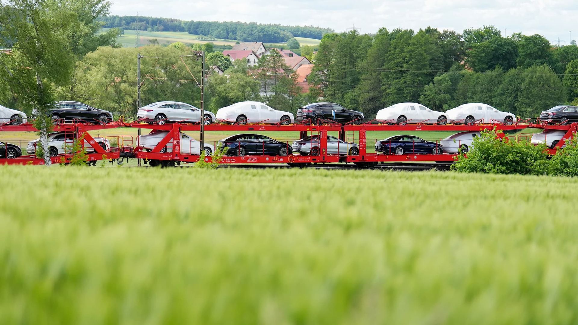 Doppelstockwagen mit Fertigfahrzeugen fahren durch grüne Landschaft.