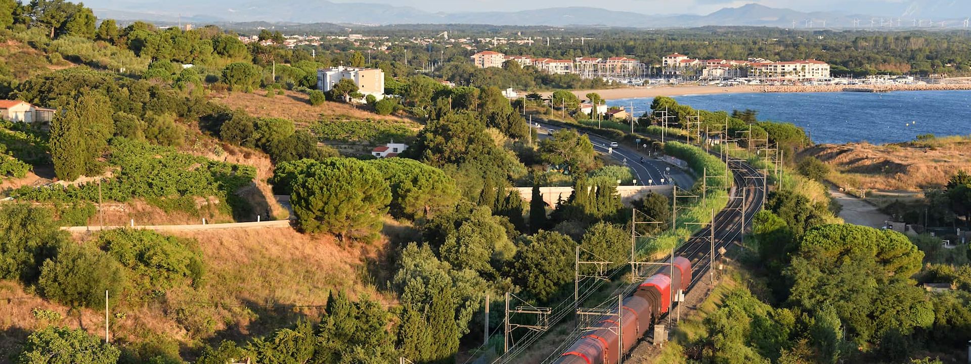 A train travels through a Mediterranean landscape.