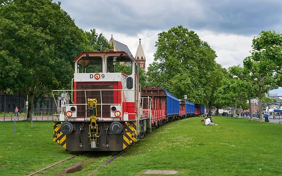 Eine Lok zieht Güterwagen am Frankfurter Mainufer.