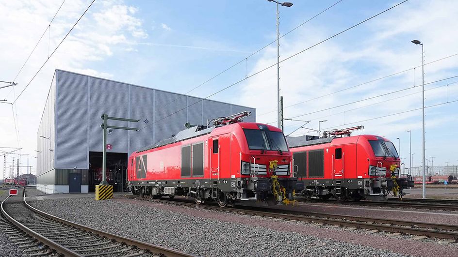 Two dual-mode locomotives next to each other in front of a maintenance shed.