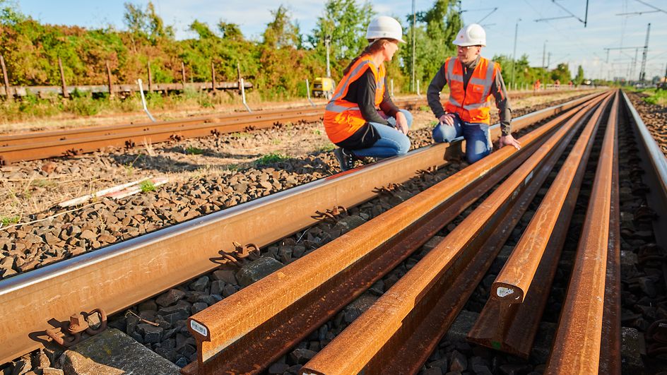 Zwei DB-Mitarbeitende hocken an den Gleisen, neue Gleise liegen vor ihnen.