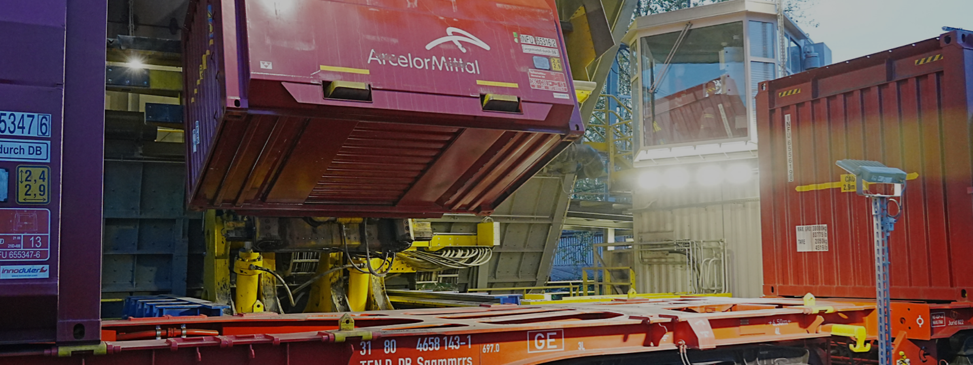 Ein roter Container wird von einer gelben Maschine auf einen Güterzug gehoben