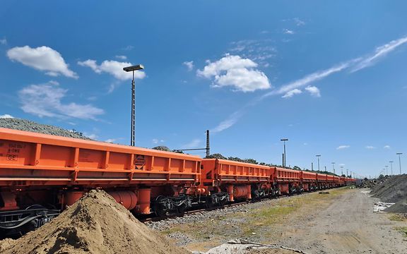 Ein Güterzug mit orangefarbenen Wagen transportieren Schotter. 