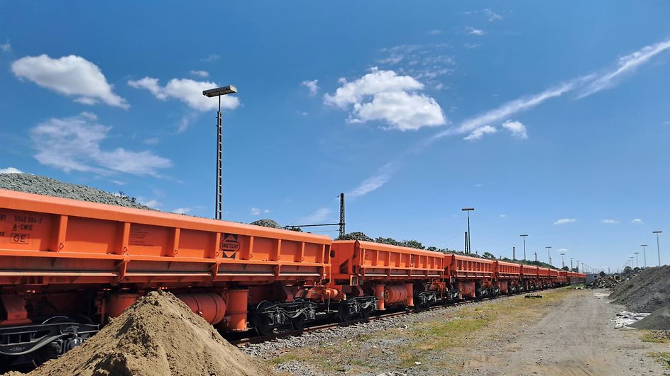 Ein Güterzug mit orangefarbenen Wagen transportieren Schotter. 