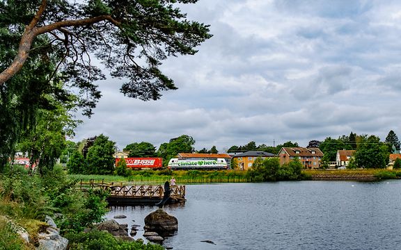 Lakescape with traditional Scandinavian houses, a freight train with the label 'climate hero' in the background