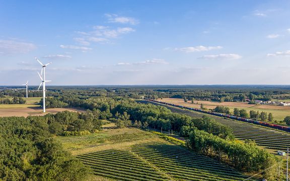 Panoramablick auf eine Landschaft mit Windkraftanlagen und einem Güterzug.