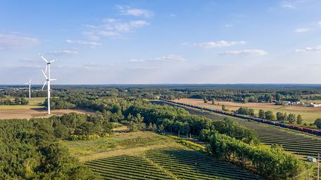 Panoramablick auf eine Landschaft mit Windkraftanlagen und einem Güterzug.