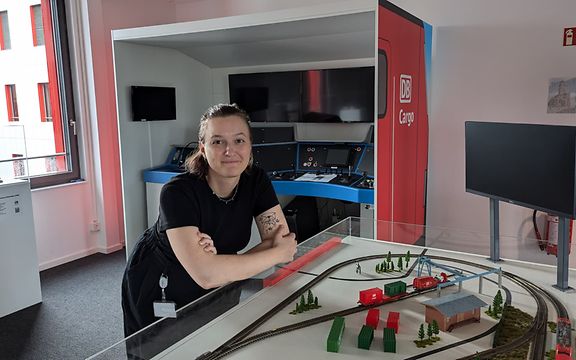 Eine Frau in dunkler Kleidung lehnt auf einer Glasvitrine mit einer Miniatureisenbahn.