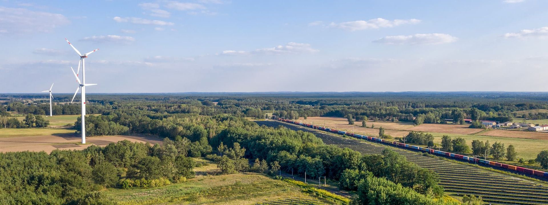 Panoramic view of a landscape with wind power plants and a freight train.