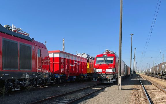 Eine Hybrid-Lok zieht mehrere Ausstellungsstücke für die InnoTrans über Gleise. Als erster Wagen ist ein Scrap-Wagen zu sehen.