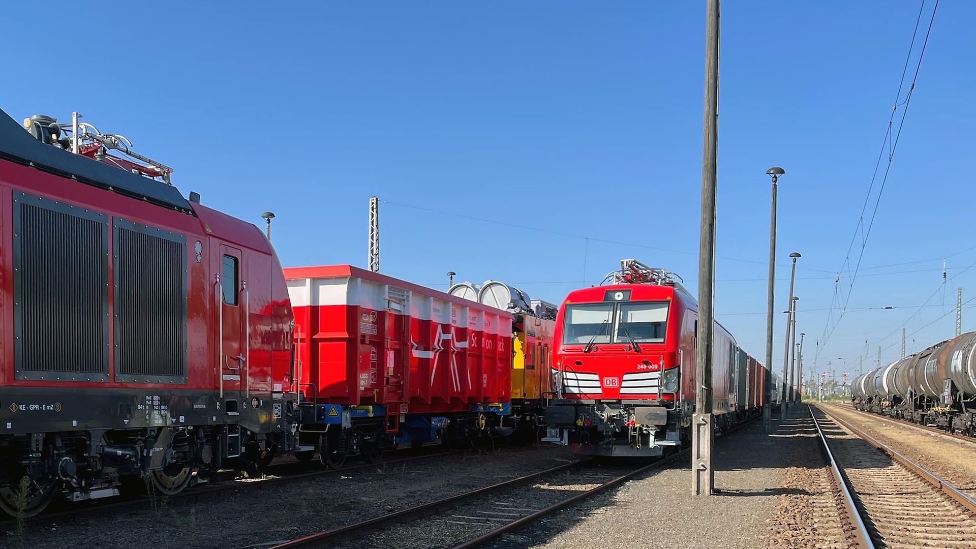 Eine Hybrid-Lok zieht mehrere Ausstellungsstücke für die InnoTrans über Gleise. Als erster Wagen ist ein Scrap-Wagen zu sehen.