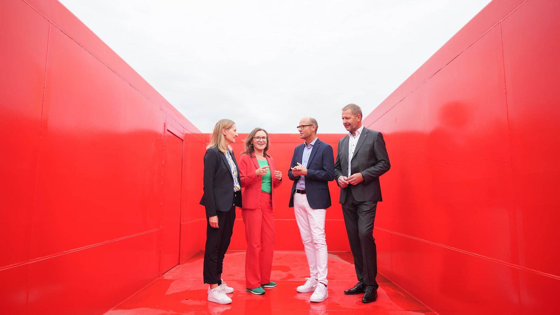 Four people are standing inside an empty red freight car for scrap logistics.