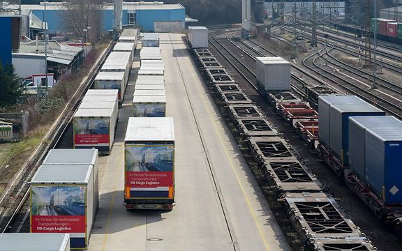 Lkw mit Containern, leere Containertragwagen und Tragwagen mit Containern stehen in einem Umschlagbahnhof nebeineinander.