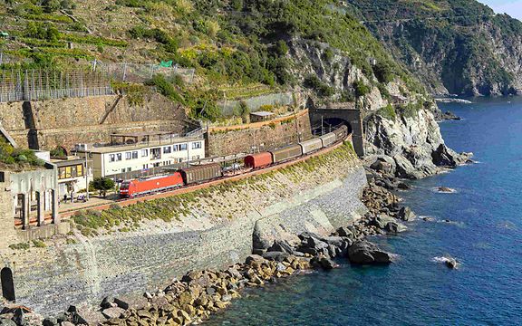 Freight train travelling along the Italian coast and just coming out of a tunnel, with the sea on the right.