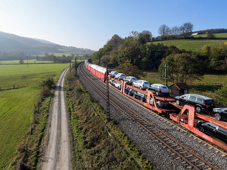 Güterzug mit beladenen Autotransportwagen fährt durch die grüne Landschaft