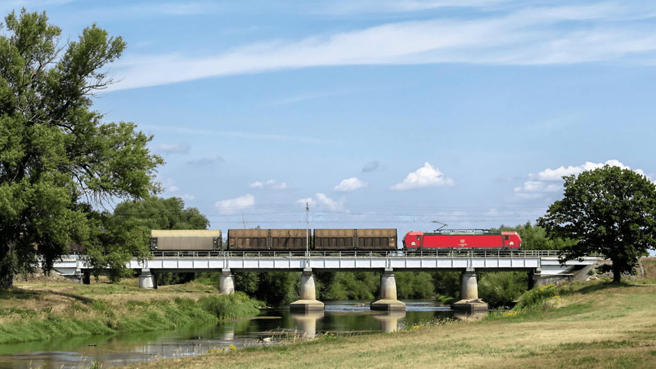 Rote Lok von DB Cargo zieht einen Zug mit Schiebewandwagen über eine Brücke