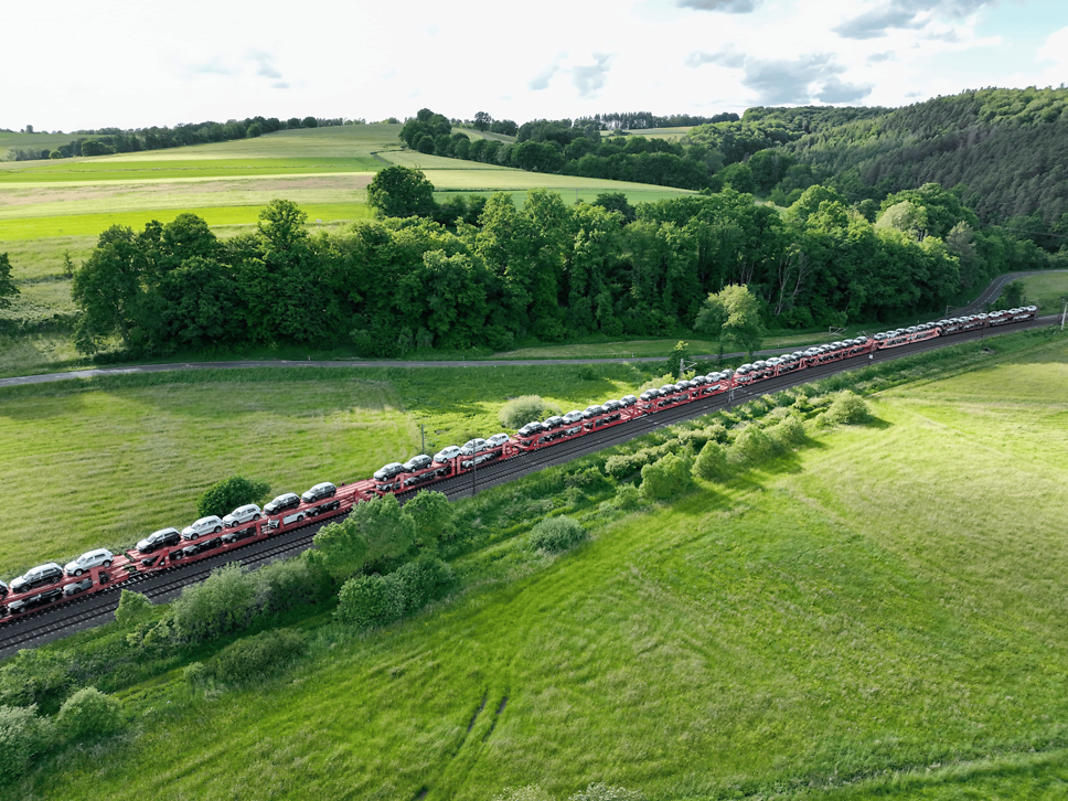 Zug mit Autotransportwagen fährt durch grüne Landschaft