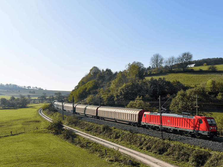 Rote Lok von DB Cargo fährt mit Schiebewandwagen durch grüne Landschaft