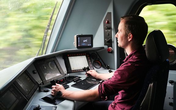 Lokführer sitzt im Führerhaus einer Lok und fährt den Zug