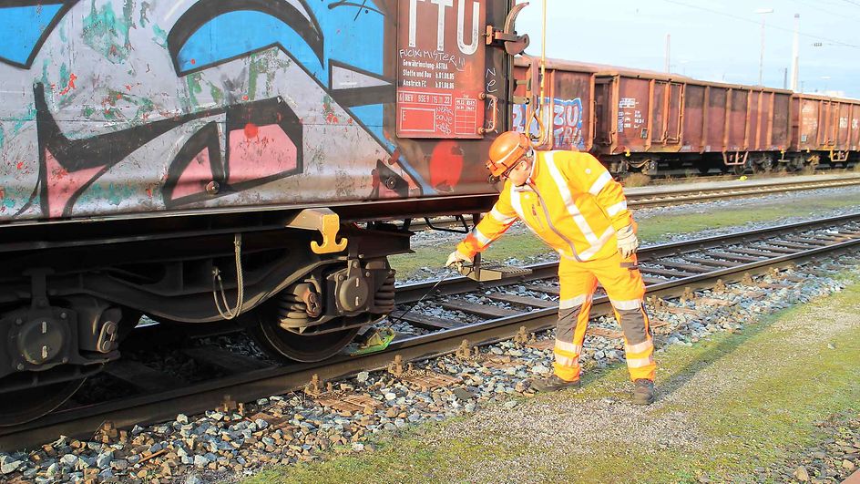 Shunting worker Sebastian Pöther stands on the siding of a slowed-down freight wagon in the marshalling yard