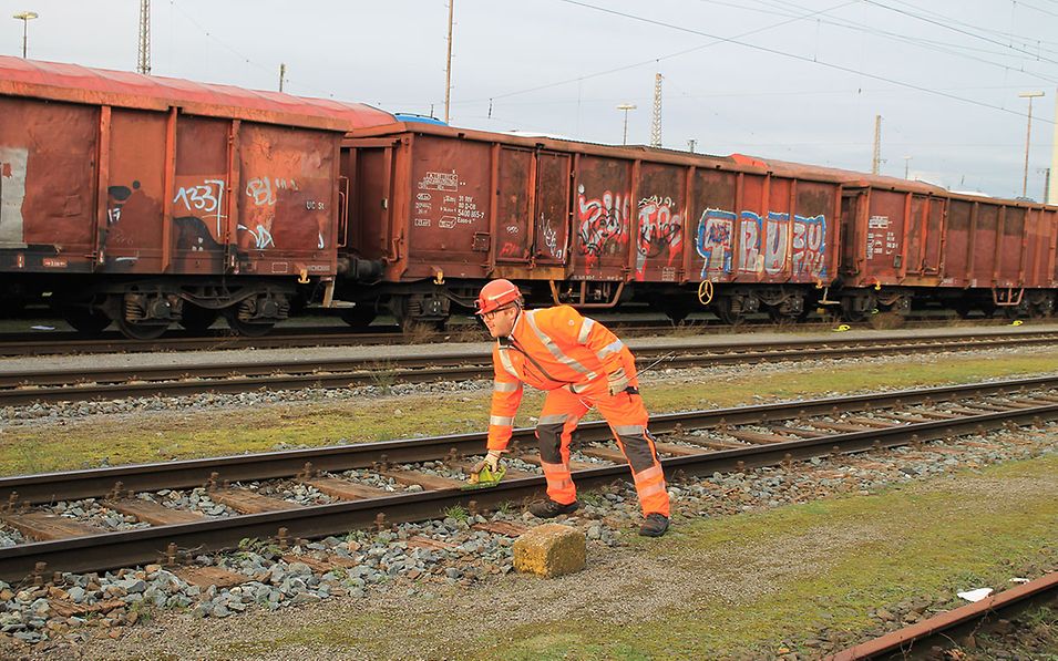 Shunting worker Sebastian Pöther stands on a track in the marshalling yard and places a brake shoe on the rails