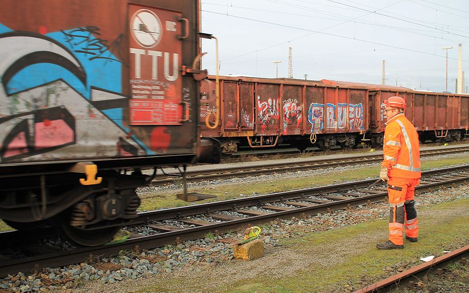 Shunting worker Sebastian Pöther is standing on a track in the marshalling yard, a freight wagon rolls onto the stop shoe