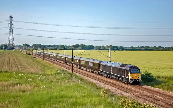 Royal train drives through a green landscape.